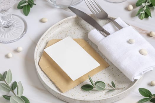 Elegant Table setting with card and envelope decorated with eucalyptus branches close up, Wedding Mockup. Romantic table with vertical paper card. Close to nature and simplicity concepts