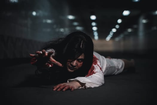 Halloween day horror concept. Asian woman zombie with blood creepy crawling move slowly creeping out, Spooky ghost tousled hair covering her face with blood in hand reach out at night time