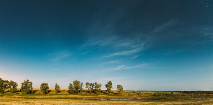 Panorama Of Blue Night Starry Sky Above Lake River. Night Glowing Stars And Trees Woods Reflected In Water. Beautiful Night Landscape With Natural Glowing Stars