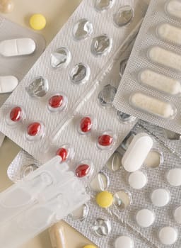Mix of pills and capsules in a aluminum and plastic blisters with some missing pills already used on light beige top view. Preventive medicine and healthcare, taking dietary supplements and vitamins