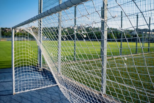 closeup of damaged soccer gate goalpost white rope net with knots and green field and blue sky in background