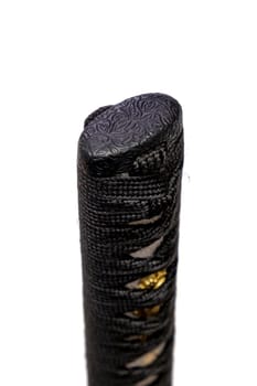 Close up the Kashira: butt cap (or pommel) made of steel on the end of the black silk cord wrapped handle Japanese sword isolated in white background. Selective focus.