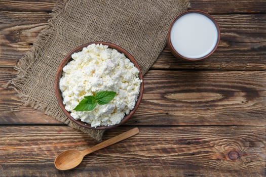 Cottage cheese and milk in clayware on wooden table, sackcloth table-napkin and wooden spoon