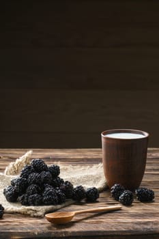Heap of fresh dewberry on sackcloth table-napkin and clay cup with milk on wooden table