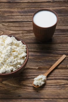 Fresh cottage cheese in  clay bowl with wooden spoon with a glass of milk on rustic wooden background