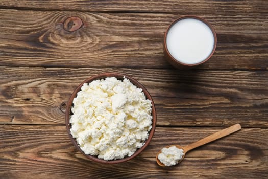 Fresh cottage cheese in  clay bowl with wooden spoon with a glass of milk on rustic wooden background
