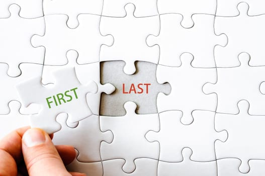 Hand with missing jigsaw puzzle piece. Word FIRST, covering  text LAST. Business concept image for completing the final puzzle piece.
