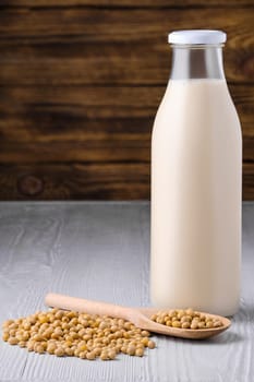 Bottle of soy milk with soybeans on white table over dark wooden background