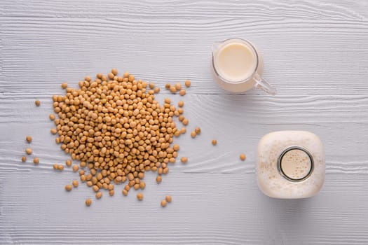 Top view of bottle and pitcher of soy milk on white wooden table