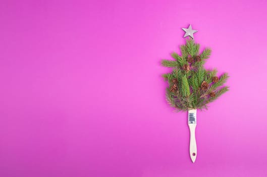 Christmas tree made from fir branches, pine cones and a painting brush as the trunk, pink greeting card with copy space