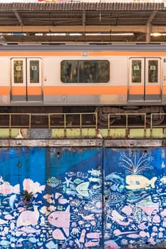 tokyo, japan - december 25 2021: Nakano Station wall decorated with children drawing of sea related fishes and shells surrounding by a JR Chuo Line train.