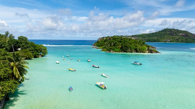 Small boats anchored on a turquoise lagoon with lush greenery surrounding the calm waters. Seychelles, Mahe.