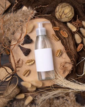 Transparent one pump bottle with liquid on wood near natural boho decorations top view, label mockup. Skincare beauty product, lotion or essence. Bohemian eco friendly cosmetics flat lay with dried leaves.