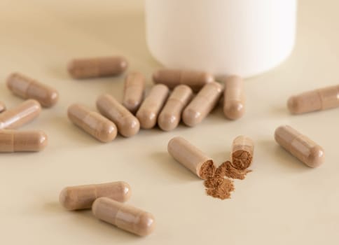 Medical capsules on light beige close up. One capsule opened to show brown powder. Preventive medicine and healthcare, taking dietary supplements and vitamins. Pharmaceutical product