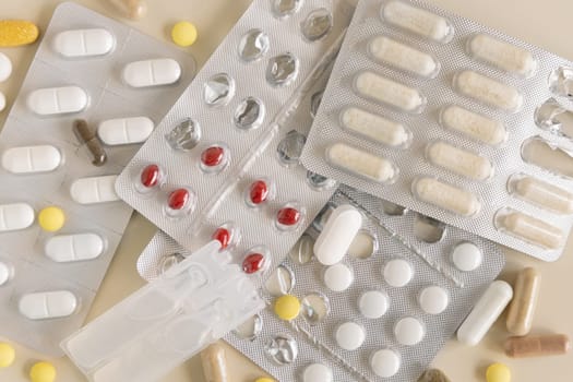Mix of pills and capsules in a aluminum and plastic blisters with some missing pills already used on light beige top view. Preventive medicine and healthcare, taking dietary supplements and vitamins