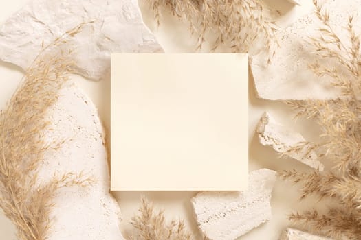 Blank card near beige travertine stones and dried pampas grass top view, mockup. Boho scene with square card. Bohemian or close to nature greeting or wedding Invitation. Close to nature.
