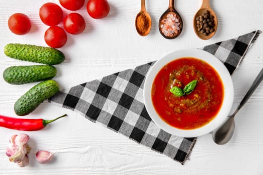 Tomato soup with basil, pepper, garlic and cucumber on wooden background. Spanish gazpacho soup.