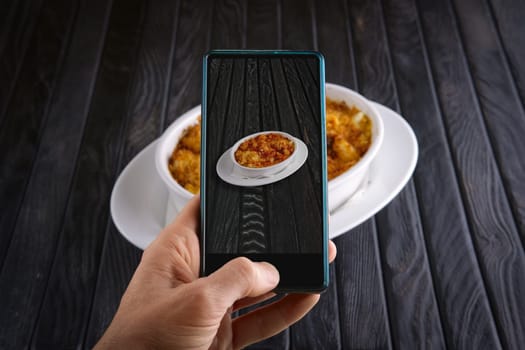 Hand with phone. Blogger making photo of food. Pasta baked with shrimps and cheese