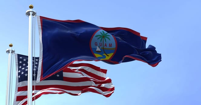 Flag of Guam waving in the wind with the US flag on a clear day. Guam is an organized, unincorporated territory of the United States in the Micronesia subregion of the western Pacific Ocean
