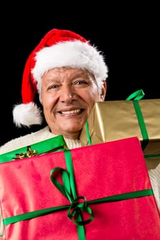 Vertical shot of merry old man carrying three differently sized gifts loaded onto his chest. Presents wrapped in gold, red and green. Kris Kringle hat. Cut-out on black. Seasonal gift giving theme.