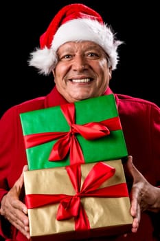 Male Senior brimming over with mirth, while handing over two foot-long presents, wrapped golden and green. Both with bowknot. Red Santa Claus cap and winter coat. Cut out on black. Gift giving theme.