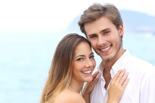 Happy couple with a white smile looking at camera on holidays on the beach isolated on white above