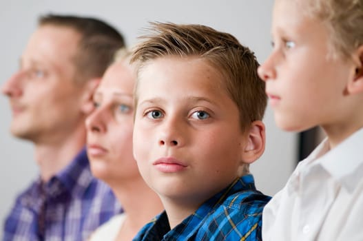 Close-up of a seven-year-old male teenager with parents and brother lined up in a fuzzy background looking seriously into the camera
