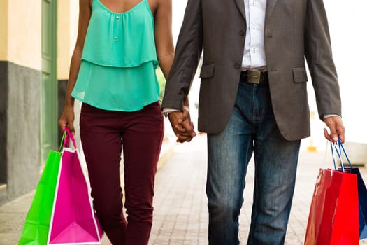 Black tourist heterosexual couple walking in the streets of Casco Antiguo in Panama City with shopping bags. Cropped view of man and woman holding hands