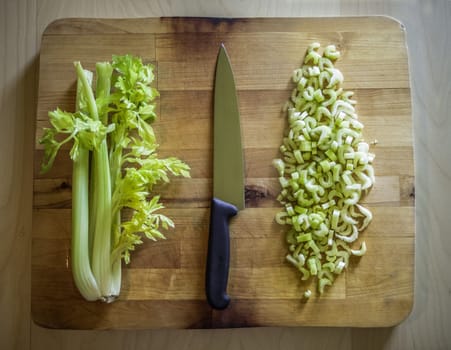 Cutted and whole celery on a wooden board with a knife