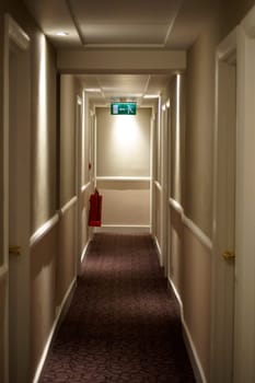 A narrow hallway with a fire extinguisher and an emergency exit.