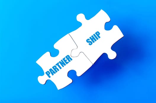 Connected puzzle pieces with word PARTNERSHIP  isolated over blue background, with copy space available. Business concept image.