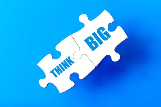 Connected puzzle pieces with text THINK BIG  isolated over blue background, with copy space available. Business concept image.