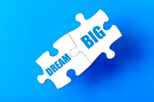 Connected puzzle pieces with text DREAM BIG  isolated over blue background, with copy space available. Business concept image.