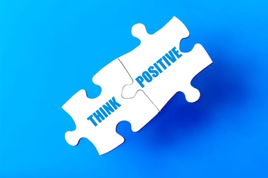 Connected puzzle pieces with text THINK POSITIVE  isolated over blue background, with copy space available. Business concept image.