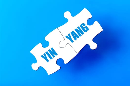 Connected puzzle pieces with words YIN YANG isolated over blue background, with copy space available. Business concept image.