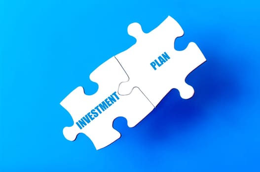 Connected puzzle pieces with words INVESTMENT and PLAN  isolated over blue background, with copy space available. Business concept image.