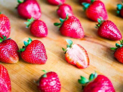 One cutted strawberry in an srranged pattern of strawberries on a wooden board, difference expression