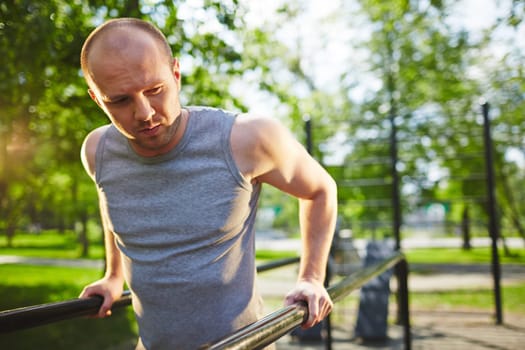 Young man in grey vest training on sport equipment outside