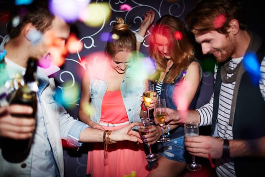 Group of young friends with flutes of champagne having party in club