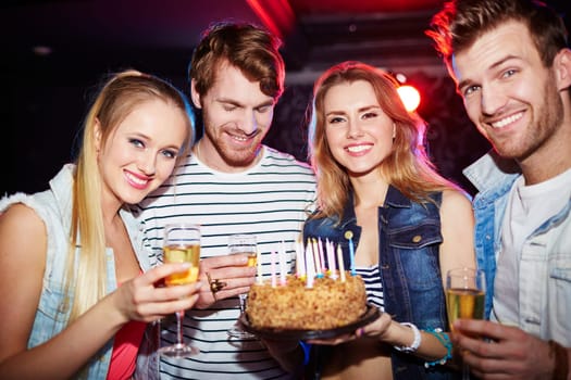 Young friends with champagne and cake looking at camera at birthday party
