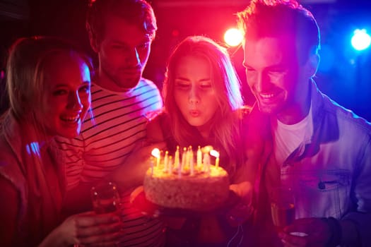 Young girl blowing candles on birthday cake between her friends