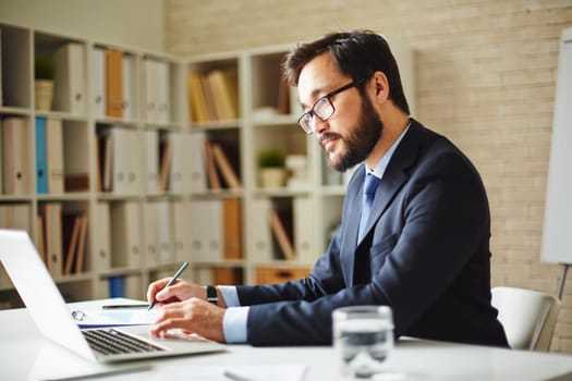 Male office worker browsing in laptop for necessary information