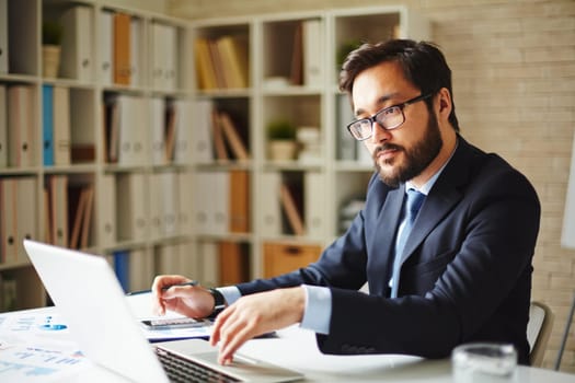 Serious businessman browsing in laptop at workplace