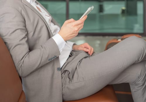 Businessman sitting at airport terminal and checking for his flight on mobile phone, waiting for plane and working while travelling