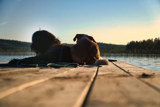 Dog lovers lying on a jetty and looking at the lake in Sweden. Goldendoodle and mixed breed. Animal friendship. Animal photo with charm.