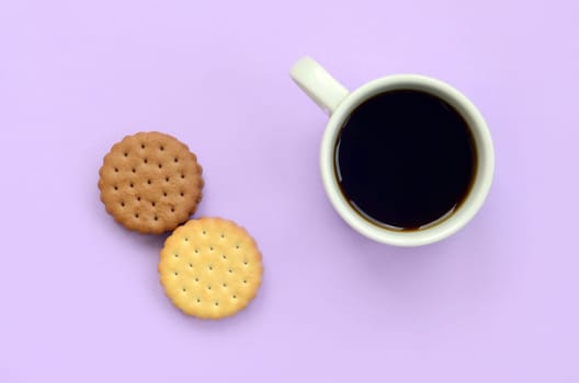 Coffee break flat lay composition with brown sandwich cookies. White hot coffee cup and brown dessert on a trendy pastel lilac background
