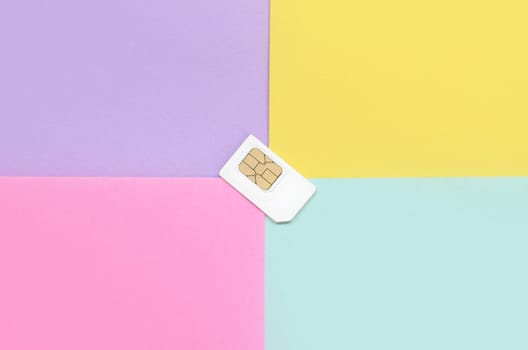 Subscriber identity module. New white SIM card on bright multicolor background. Minimal flat lay top view. Violet, pink, yellow and blue pastel colors