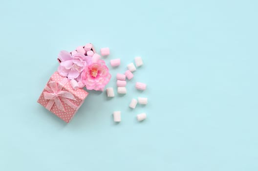 Flowered pink gift box sprinkled with marshmallows on blue background. Metaphorical concept processing and cultivation of flowers. Minimalism flat lay. Top view