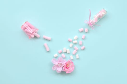 Metaphorical concept of care for flowers. Pink flower sprayed with marshmallows from small transparent tanks on a pastel blue background. Minimal flat lay composition. Top view