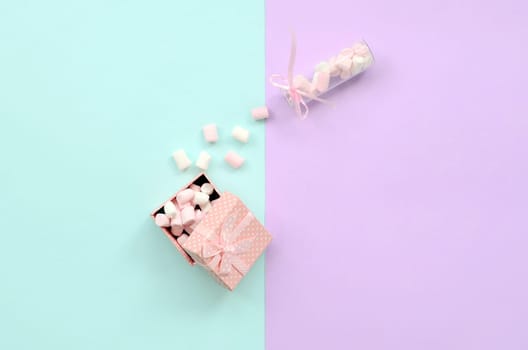 A marshmallow from a glass jar fills a pink gift box on a colored pastel blue and violet background. Minimalism flat lay. Top view